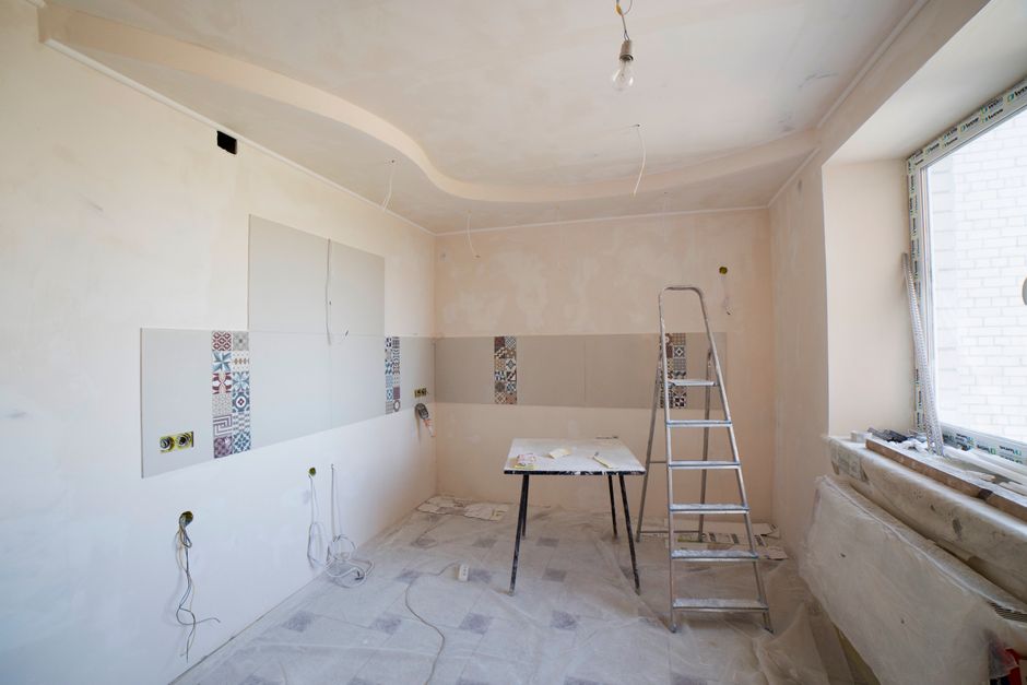 A male construction worker operating a concrete mixer during an after builders cleaning process in a renovation project at a residential property in Holland Park W8. The room is in the midst of development, with unfinished walls, visible scaffolding, and construction materials scattered on the floor. Bright natural light streams through a large window, illuminating the space. The worker, dressed in casual clothing and white gloves, focuses on pouring or mixing materials, with a white bucket and packaging of construction supplies nearby. Cleaners W8 provides comprehensive cleaning services to restore hygiene and surface cleanliness after builders work, ensuring floors, surfaces, and fixtures like wood and tiled areas are free from dust, debris, and residual materials, suitable for both domestic and commercial settings.